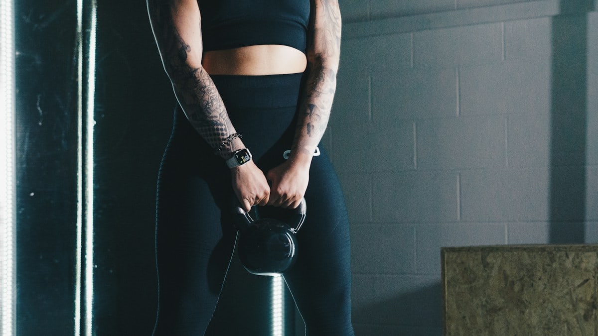 a woman with tattoos holding a kettle in a gym